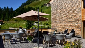 An outdoor patio with tables and chairs, a large umbrella, and a brick wall.