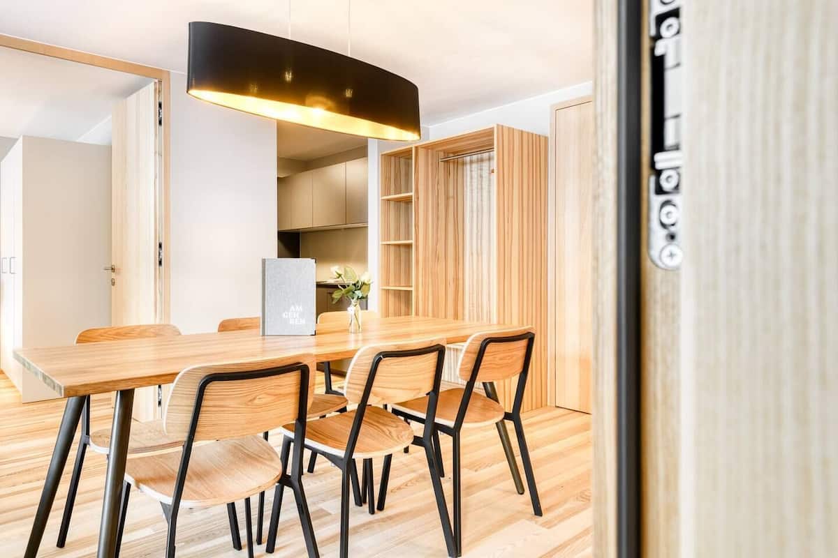 A modern dining area with a wooden table and chairs, a pendant light, and a bookshelf.