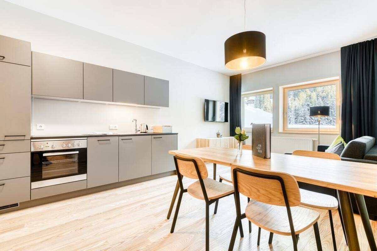 A modern kitchen with grey cabinets, a wooden dining table, and a large window with a view of trees.