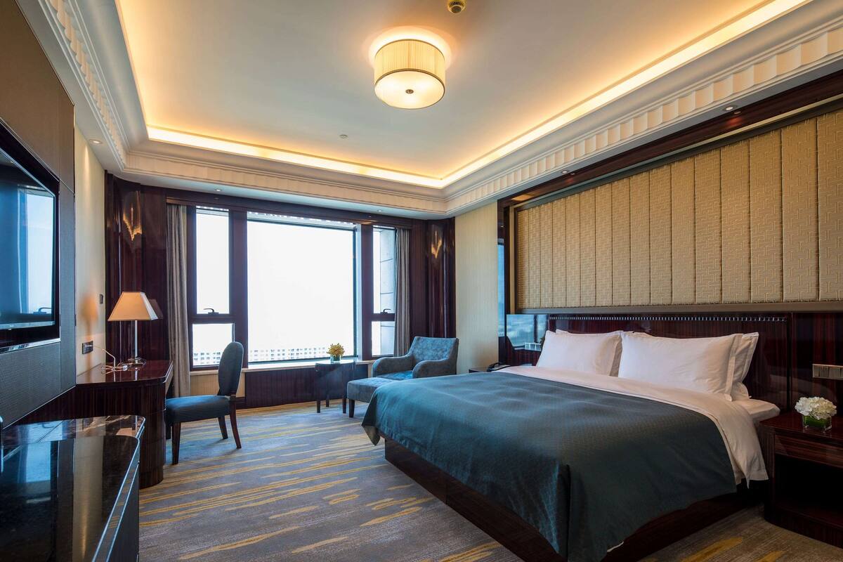 A hotel room with a large bed, a desk with a lamp, a chair, and a TV.