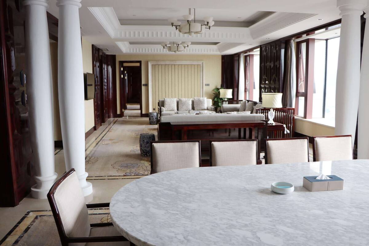 A spacious room with a round marble table, a sofa set, and a large window with curtains.
