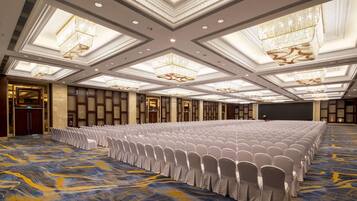 Un salón de conferencias amplio con filas de sillas blancas, una alfombra estampada y candelabros ornamentados.