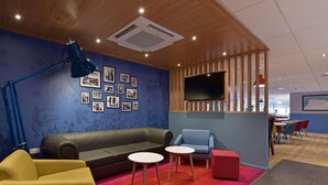 A modern lounge area with a sofa, chairs, a small table, and a TV. - Travelodge Plus Edinburgh Park (Edinburgh)