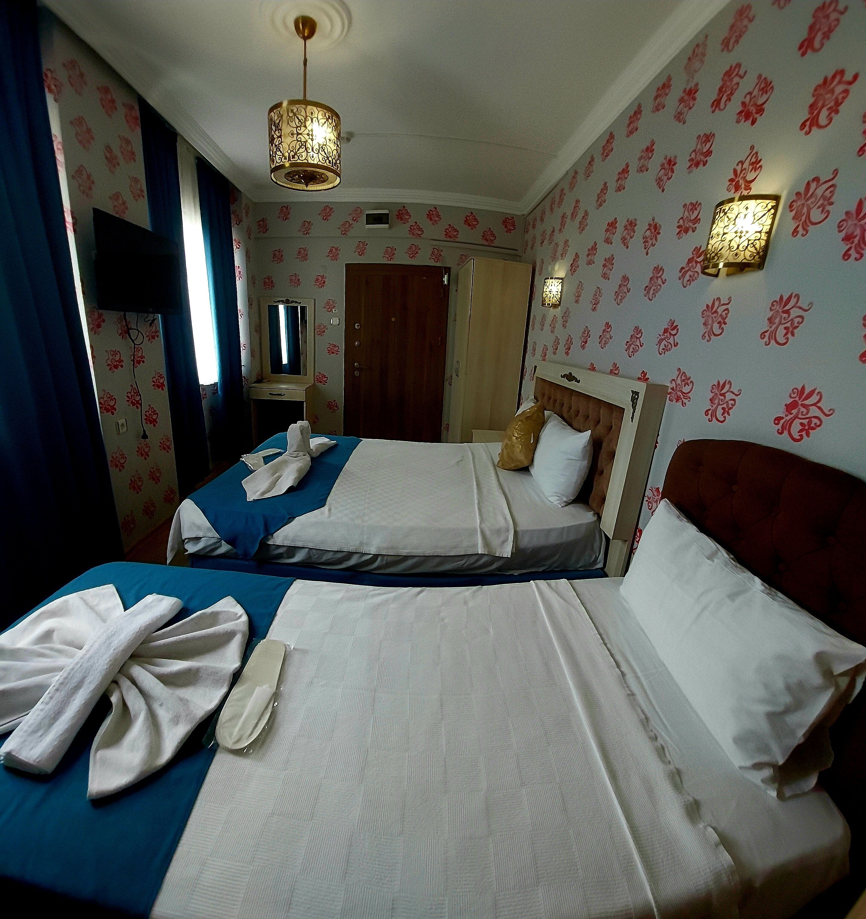 A hotel room with two beds, a mirror, a wardrobe, and a hanging light fixture.