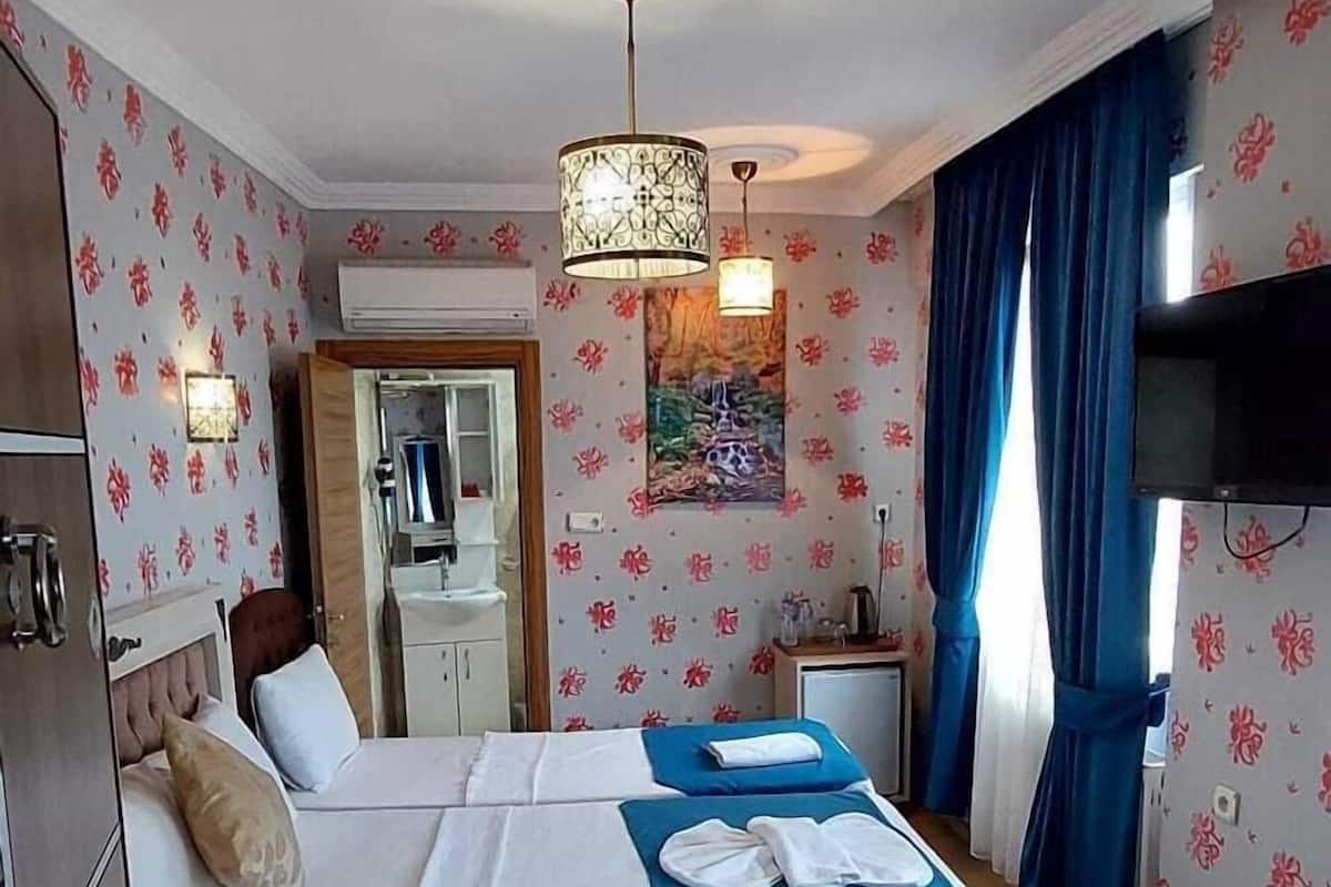 A hotel room with a bed, wardrobe, mirror, and a small table with a lamp.
