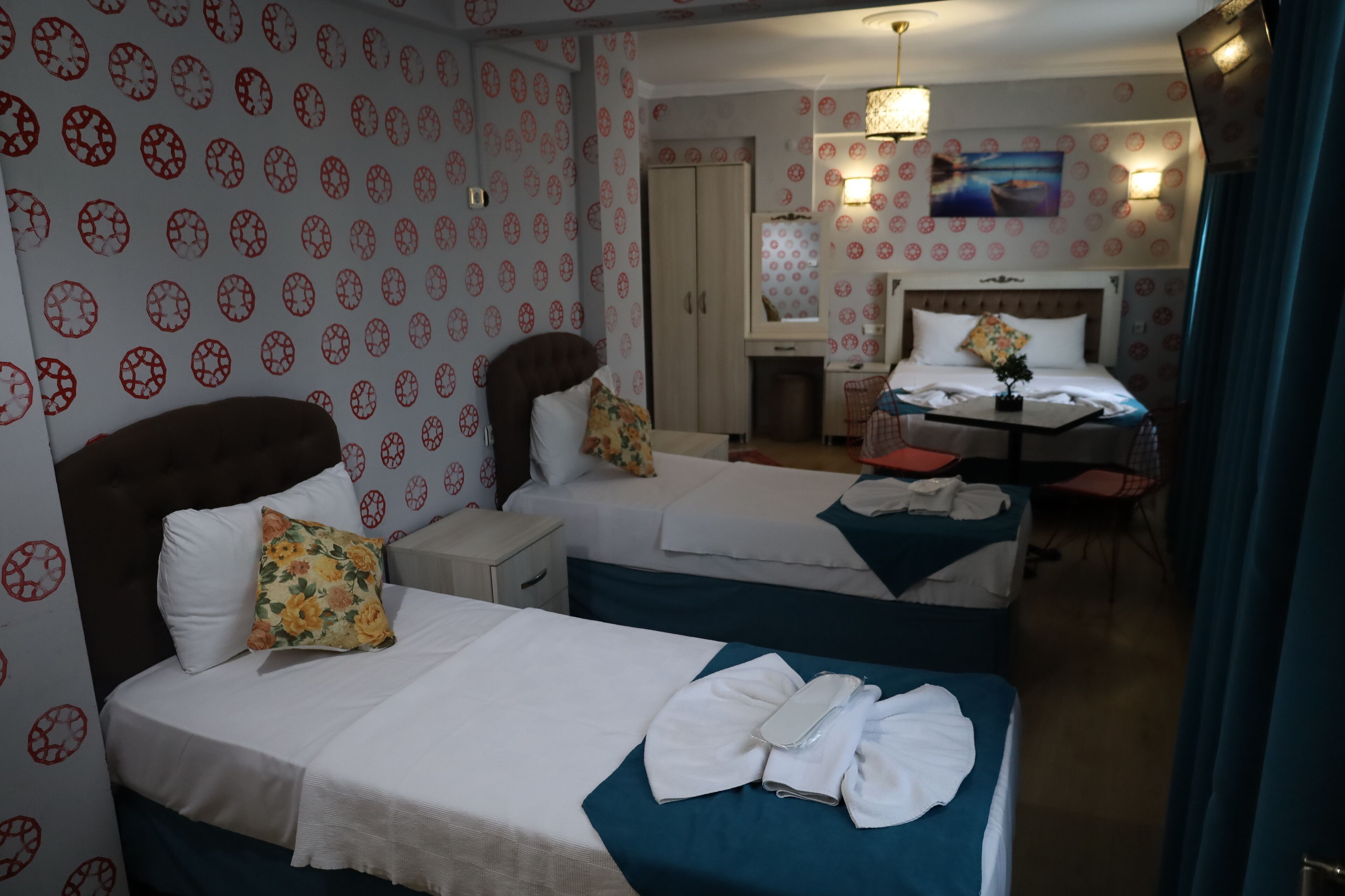 A hotel room with two beds, a desk, and a chair. There is a wardrobe and a painting on the wall.
