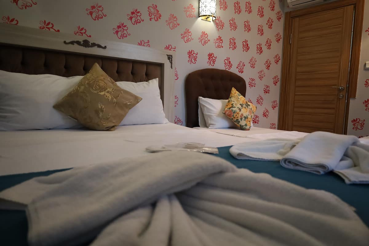 A hotel room with a large bed, two pillows, a bedside table, and a wooden door.