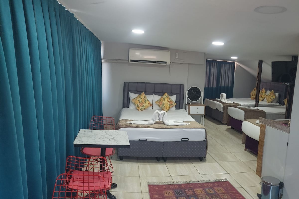 A hotel room with a bed, a small table, a chair, a sofa, a mirror, and an air conditioning unit.