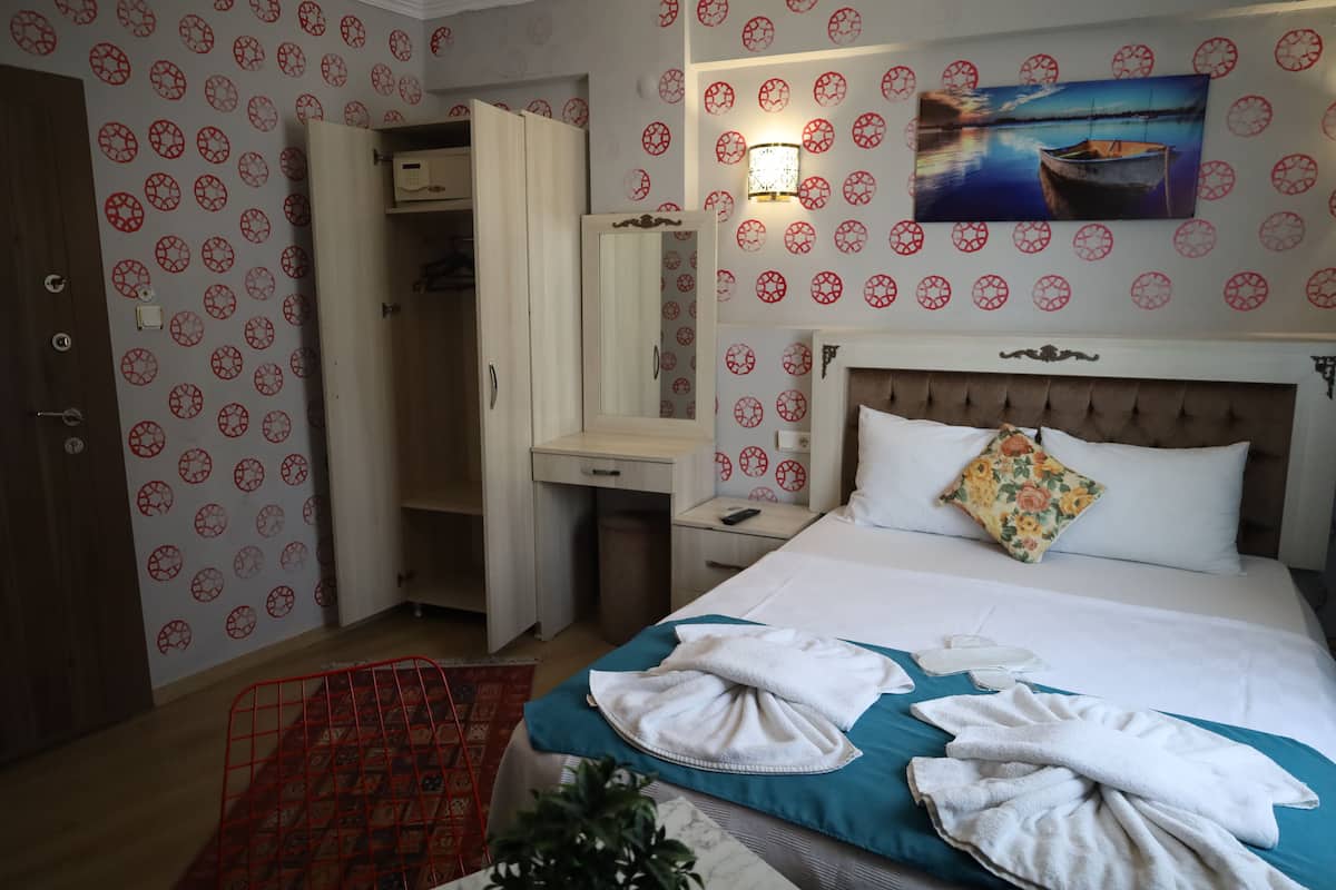 A hotel room with a bed, a desk, a wardrobe, and a painting on the wall.