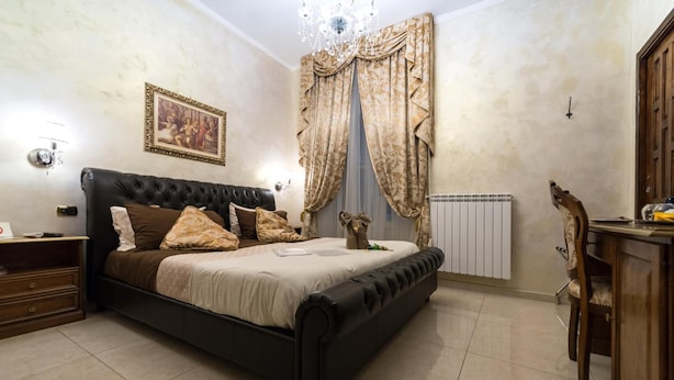 A bedroom with a large bed, a wooden nightstand, a dresser, a radiator, and a chandelier. - Roma Royal Residence (Rome)