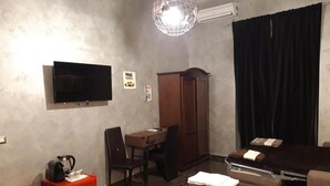 A compact hotel room with a flat-screen TV, a desk with a chair, a wardrobe, a sofa, a small table with a coffee maker, and a J&B whisky barrel. - Roma Royal Residence (Rome)