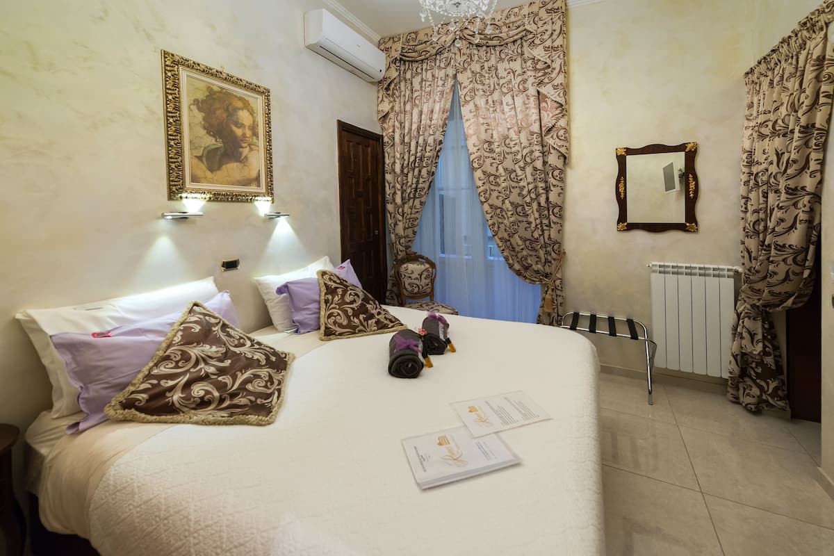 A hotel room with a bed, pillows, a framed picture, a mirror, and a radiator.
