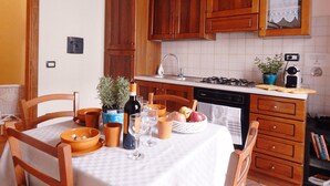 A kitchen with wooden cabinets, a stove, and a dining table set with bowls, wine glasses, and a fruit basket. - Cozy apartment near Chatedral and Medici Chapels (Firenze)