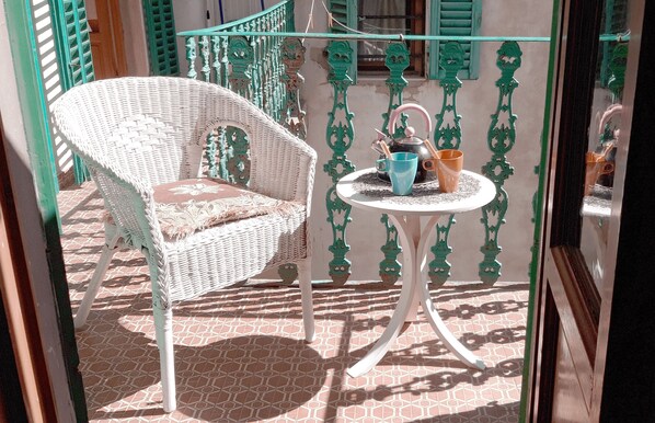 Une chaise en osier et une petite table ronde sur laquelle se trouvent une théière et des tasses, le tout placé sur une terrasse carrelée.