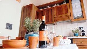 A kitchen with wooden cabinets, a table with a bottle of wine, a glass, and various kitchen items. - Cozy apartment near Chatedral and Medici Chapels (Firenze)