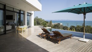 A modern outdoor area with a wooden deck, a pool, and a view of the sea. - The Cliff House (Carthage)