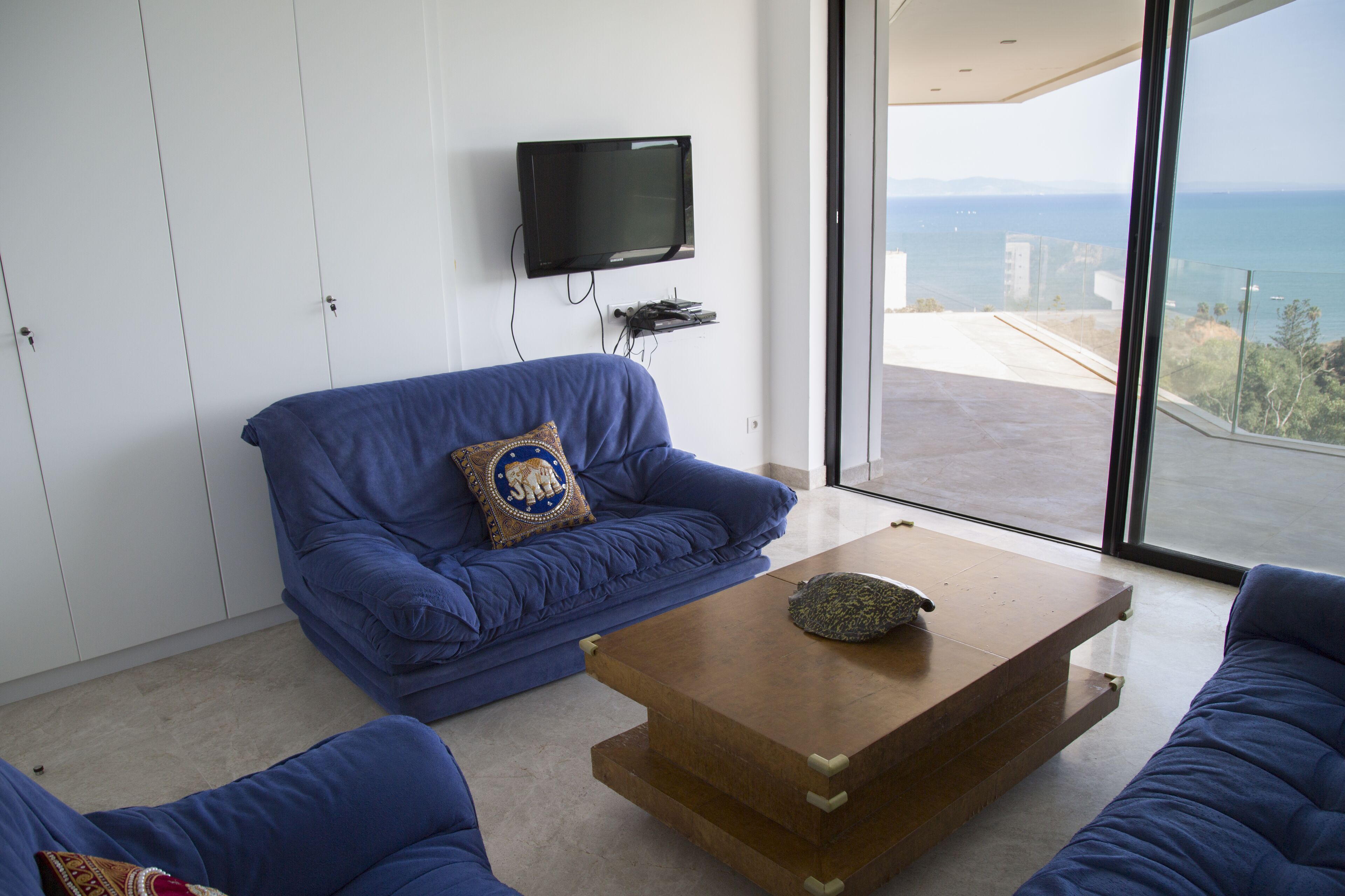 A modern living room with a blue sofa, a wooden coffee table, and a television mounted on the wall.