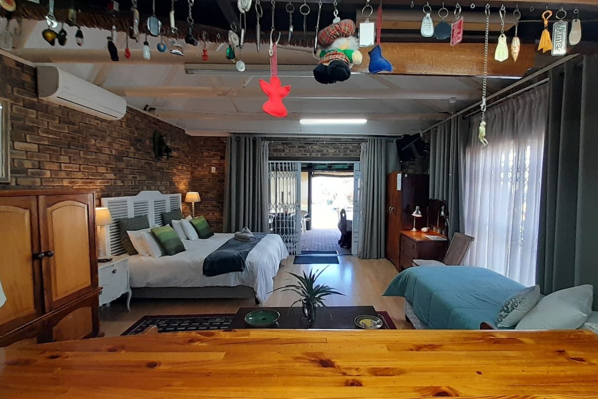 A cozy hotel room with a brick wall, a bed with a wooden headboard, a desk with a lamp, and a view of the outside.