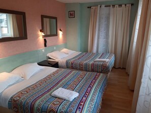 Habitación de hotel con dos camas, cada una con ropa de cama estampada, cabecero, mesita de noche, espejo y ventana con cortinas.