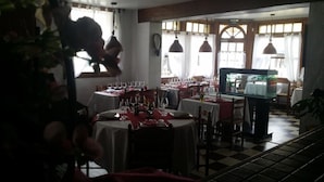 A restaurant with multiple tables set for dining, a fish tank in the corner, and large windows with curtains. - Hotellerie Normande (Dozule)