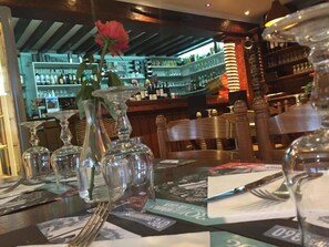 A bar area with a wooden ceiling, shelves stocked with bottles, and a rose in a glass vase on the table. - Hotellerie Normande (Dozule)