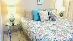 Un dormitorio con una cama, dos mesitas de noche, un cuadro en la pared y una ventana con cortinas.