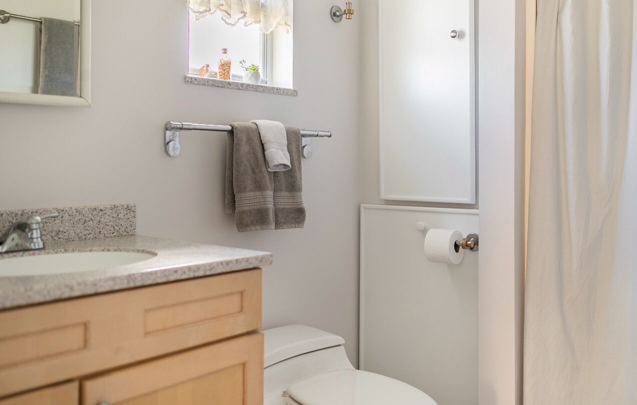 Ein Badezimmer mit Waschbecken, Spiegel, Handtuchhalter, Toilette und einem Fenster mit Vorhängen.