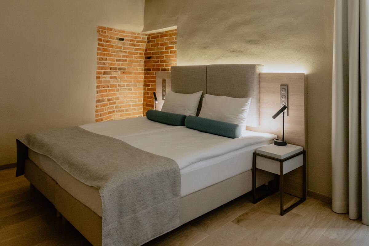 Un dormitorio con una cama, una mesita de noche, una lámpara, un muro de ladrillo y un techo de madera.