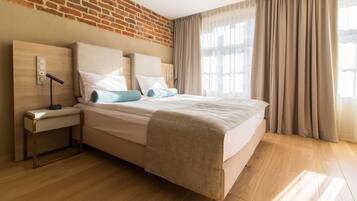 Ett modernt hotellrum med en tegelvägg, ett trägolv, en säng med beige sängkläder, ett nattduksbord med en lampa och ett fönster med gardiner.