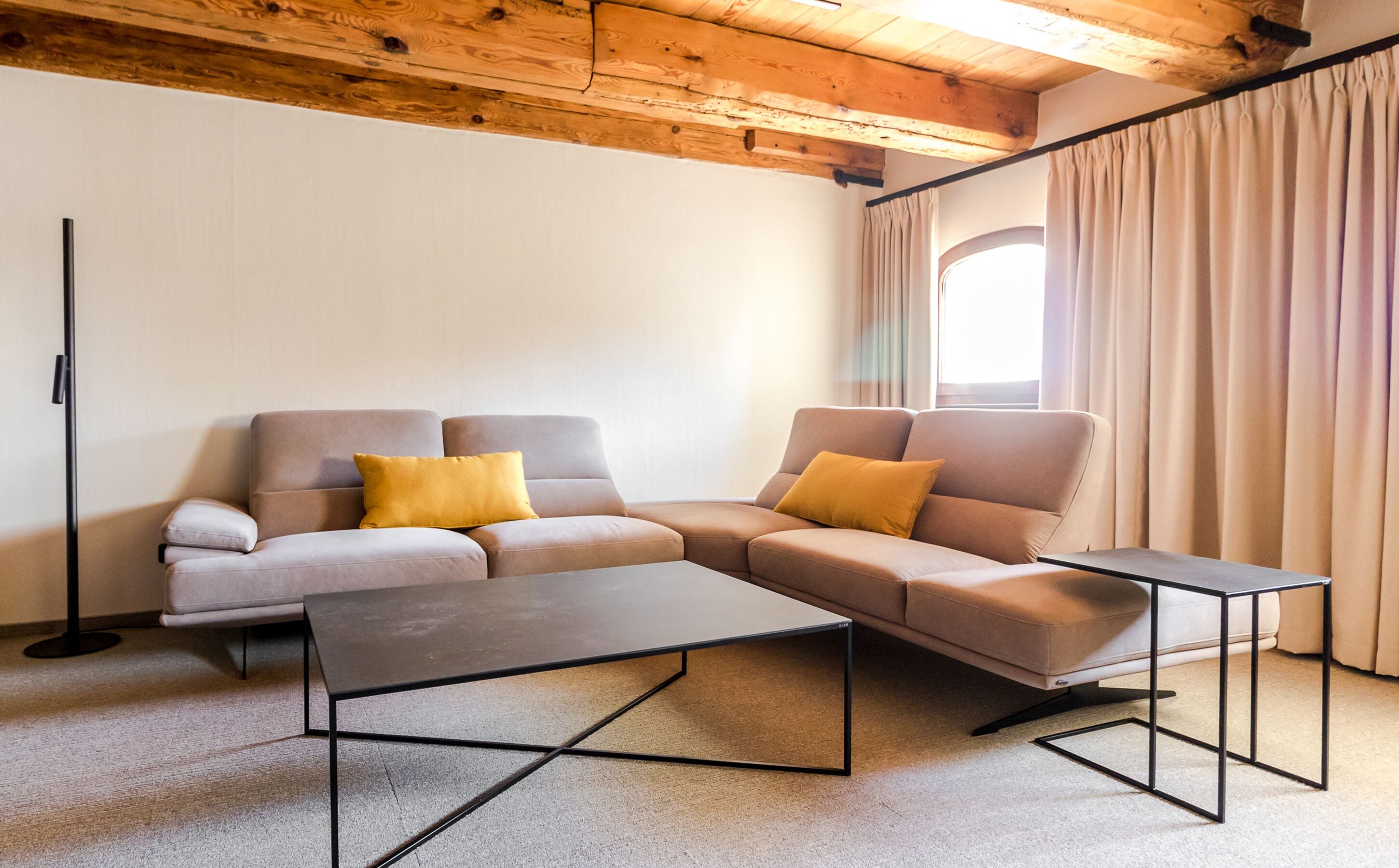 Una sala de estar moderna con un sofá modular, dos mesas auxiliares y un techo de madera.
