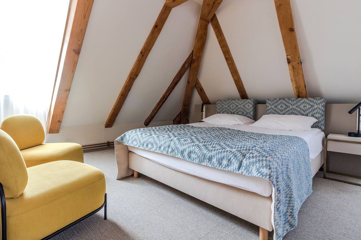Un dormitorio con una cama, un sillón amarillo y una estructura de techo de madera.