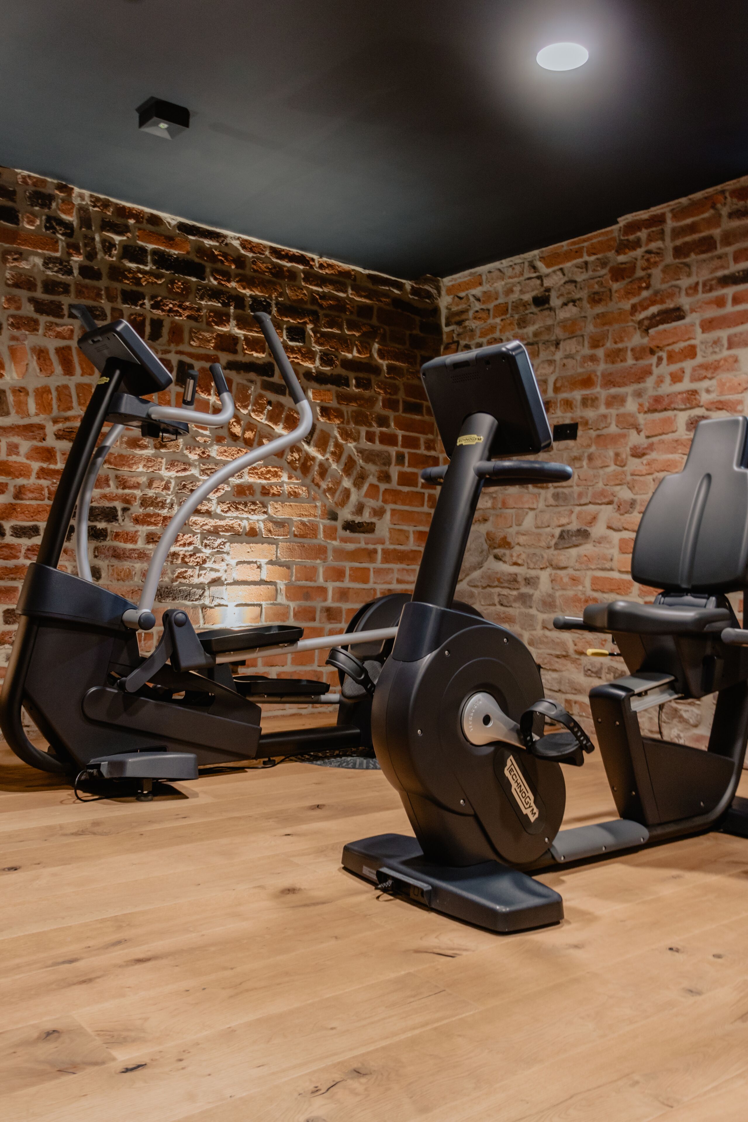 Un gimnasio con equipo de ejercicio, una pared de ladrillo y suelo de madera.