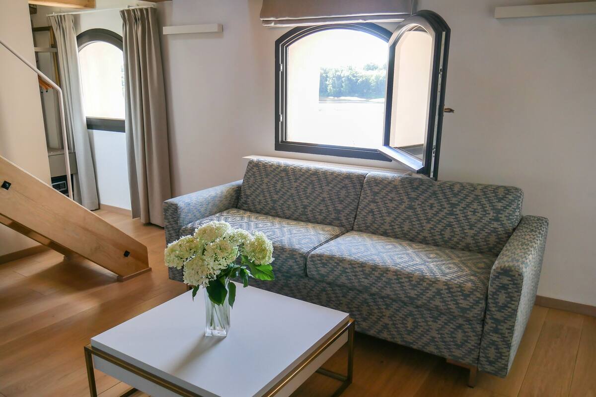 Una sala de estar con un sofá estampado, una mesa de centro blanca y un florero con flores.