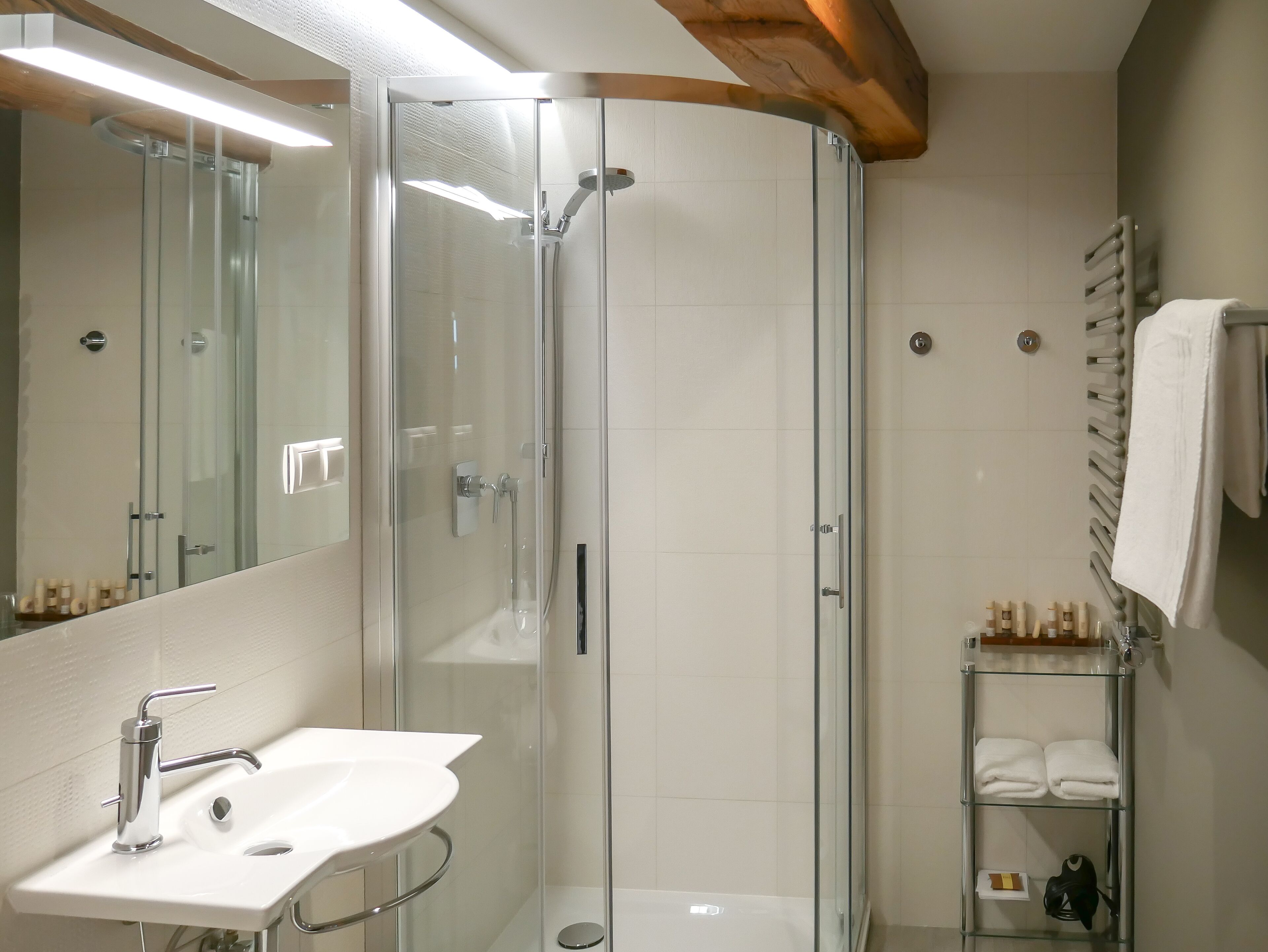 Un baño moderno con ducha de vidrio, un lavamanos blanco con accesorios cromados y un perchero con toallas dobladas.
