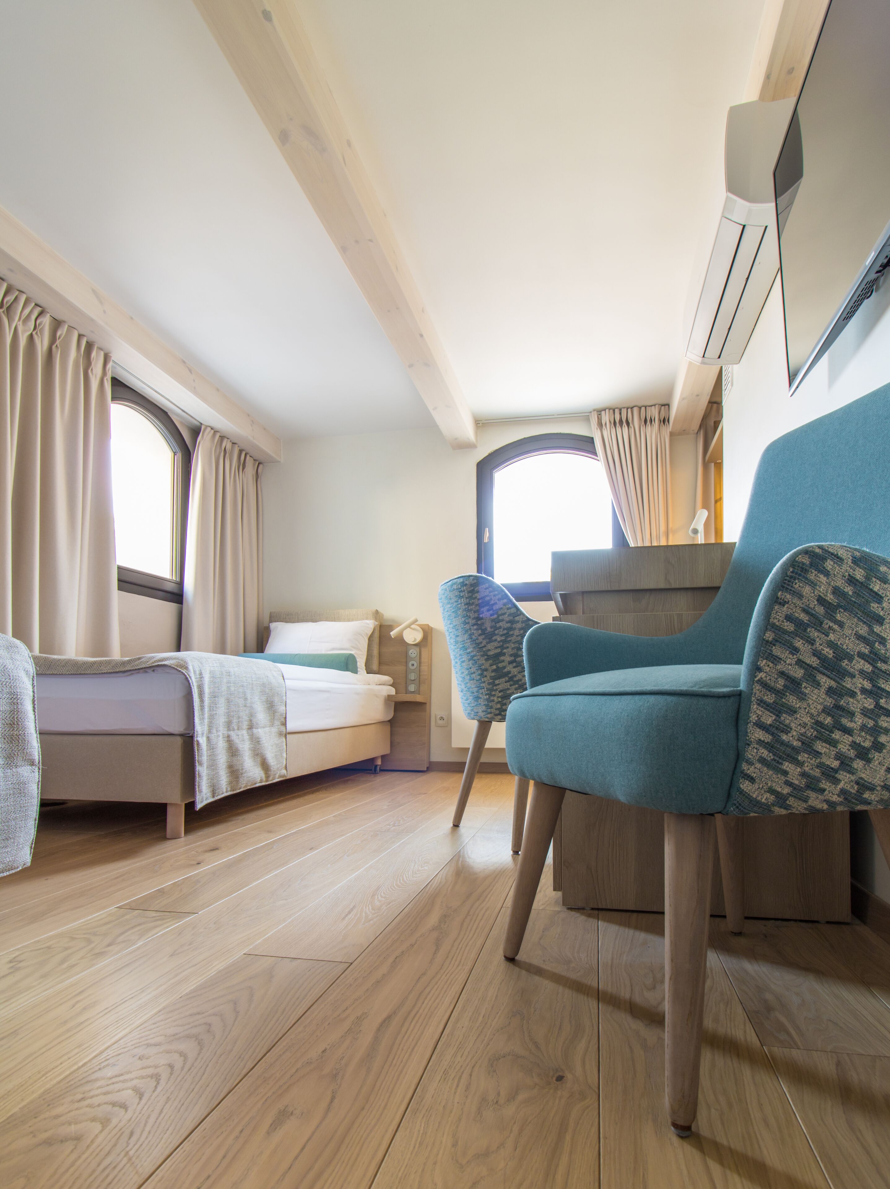 Una habitación pequeña con cama, una silla, un escritorio y un ventanal.