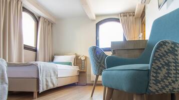 Una habitación pequeña con cama, una silla, un escritorio y un ventanal.