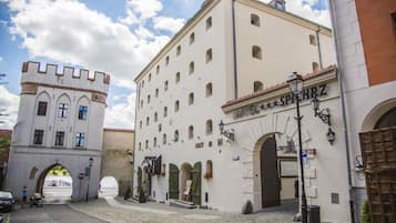 A historic building with a castle-like tower, arched doorways, and a sign reading "SPIEHHRZ".