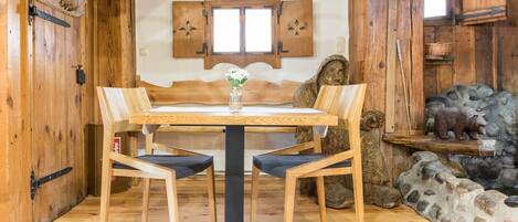 A wooden dining table with four chairs, a vase with flowers, and rustic decor including a bear sculpture and a stone wall.