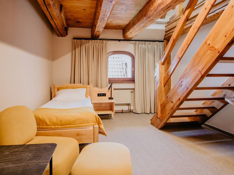 A cozy room with a bed, two chairs, a desk, and a window with curtains.