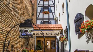 Un callejón estrecho con un pub llamado "REZMI SPICHRZ" y un edificio de ladrillo con jardineras florales.
