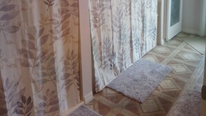A hallway with patterned curtains, a door, and a tiled floor with rugs. - CLEAN, COMFORTABLE, FULLY PRIVATE UNIT IN GATED COMMUNITY  (Ocala)