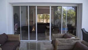 A modern living area with a glass sliding door leading to an outdoor patio. Inside, there are wicker sofas and a glass coffee table. - Villa Malaga (Carthage)