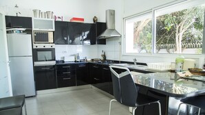 A modern kitchen with black cabinets, a stainless steel refrigerator, a built-in oven, and a large window providing a view of trees. - Villa Malaga (Carthage)