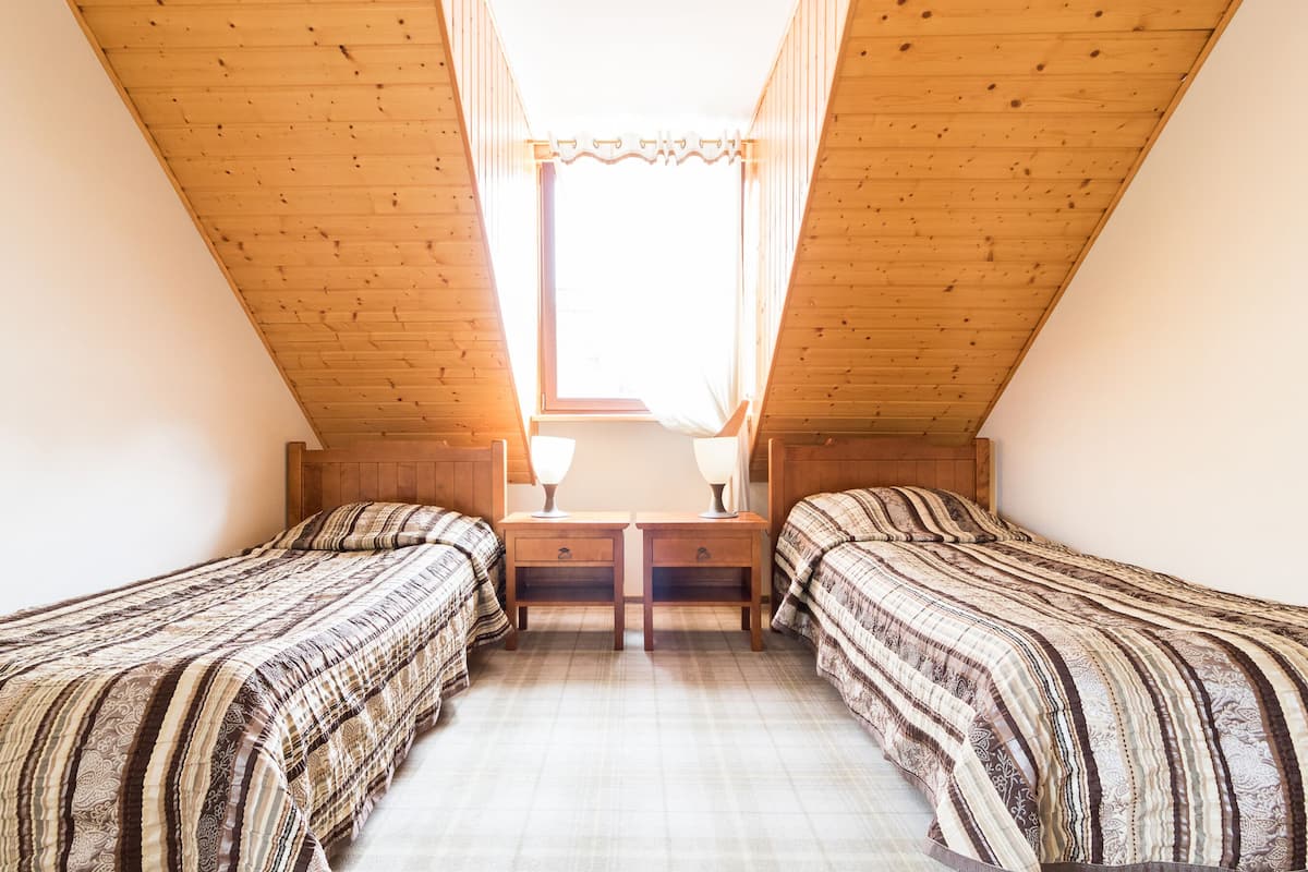 Una habitación pequeña y acogedora con dos camas, una ventana con cortinas y techo de madera.