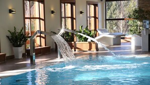Une piscine agrémentée d’une cascade, entourée de chaises longues et de plantes en pot.