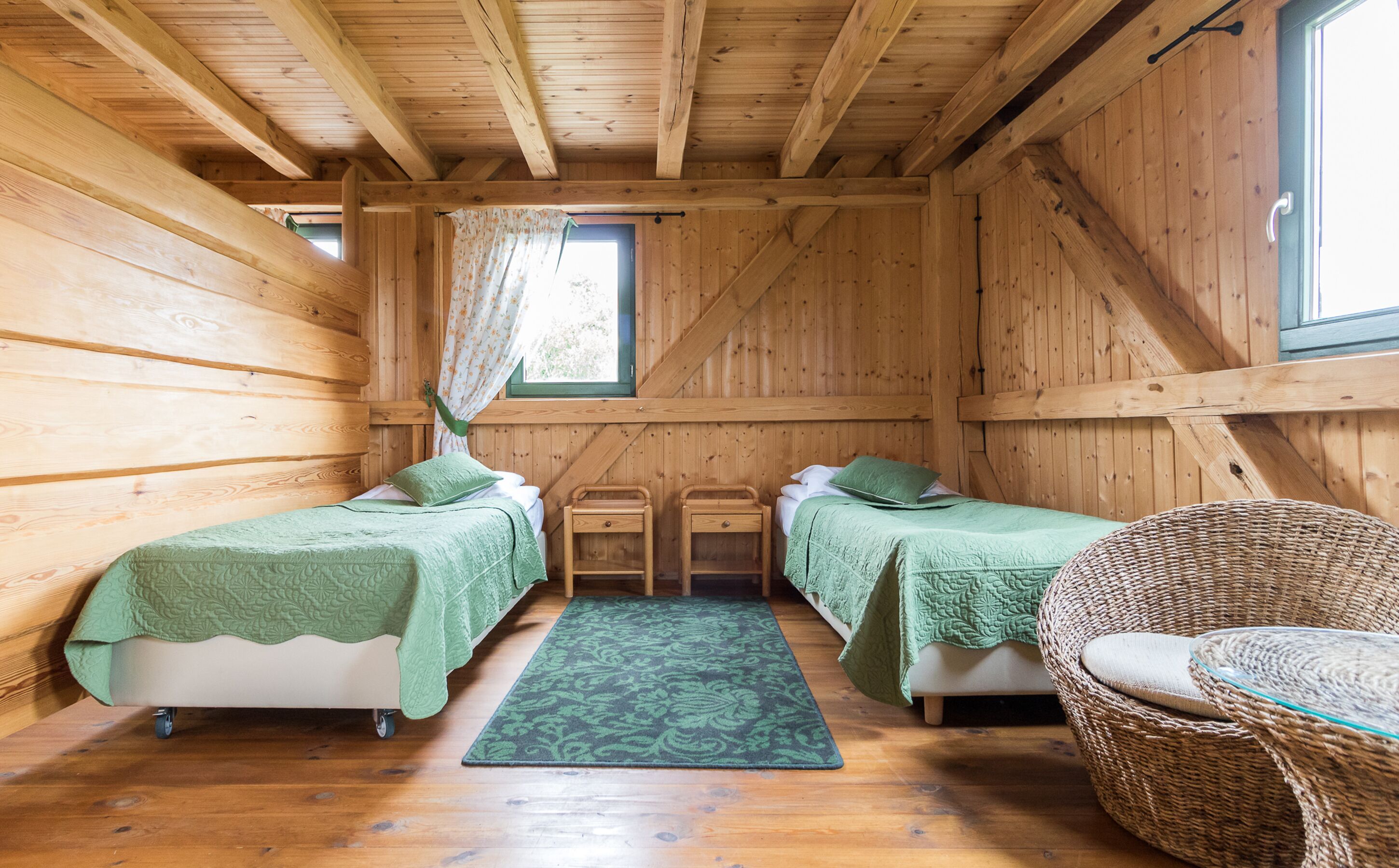 Een houten kamer met twee bedden, een rieten stoel en een raam met gordijnen.