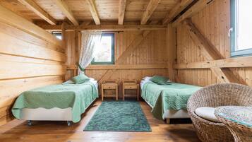 Een houten kamer met twee bedden, een rieten stoel en een raam met gordijnen.