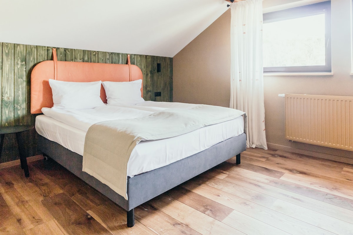 Un dormitorio con cama, suelo de madera y ventana con cortinas.