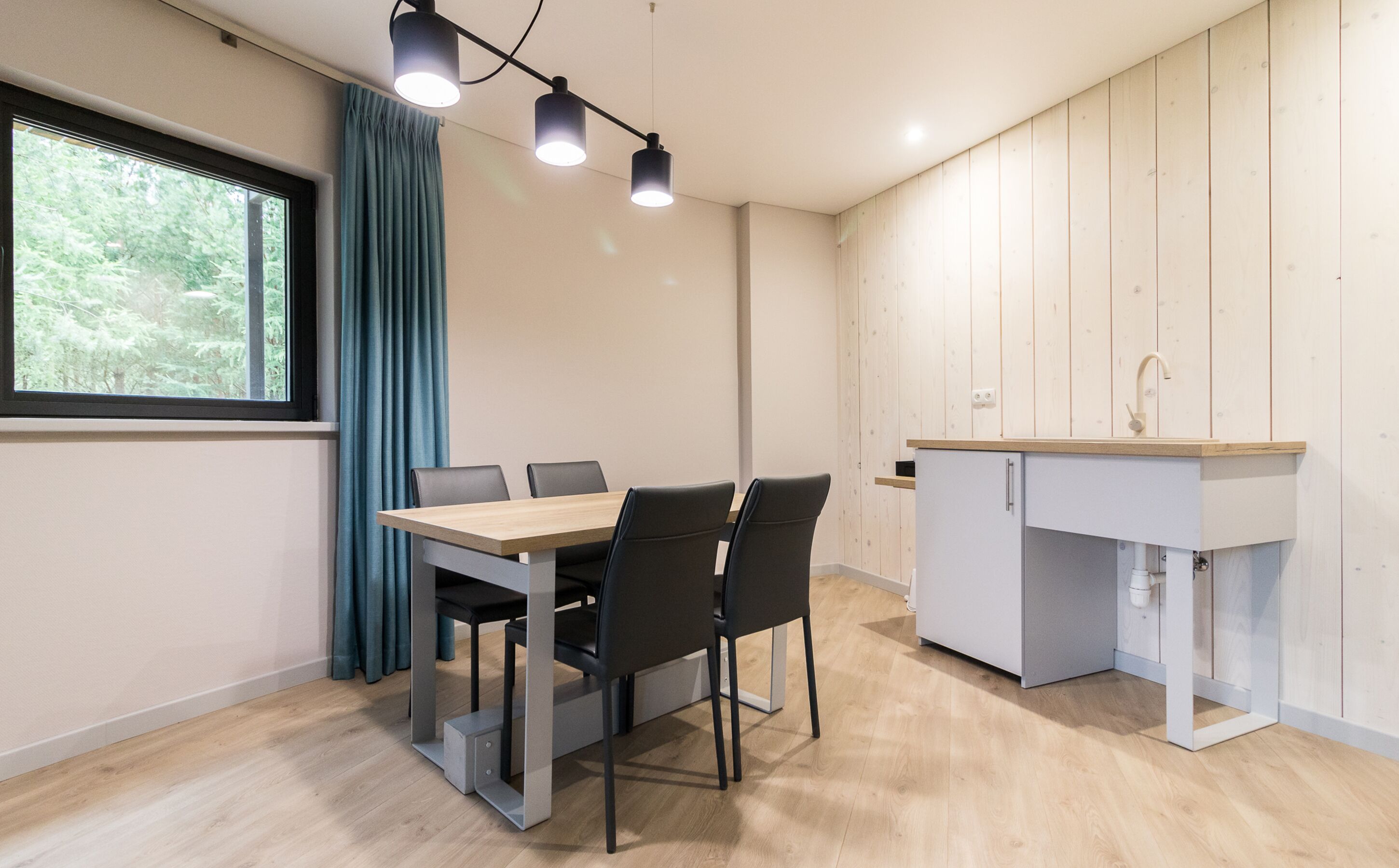 A modern kitchen with a wooden countertop and a built-in sink. There is a dining table with chairs and a window with curtains.