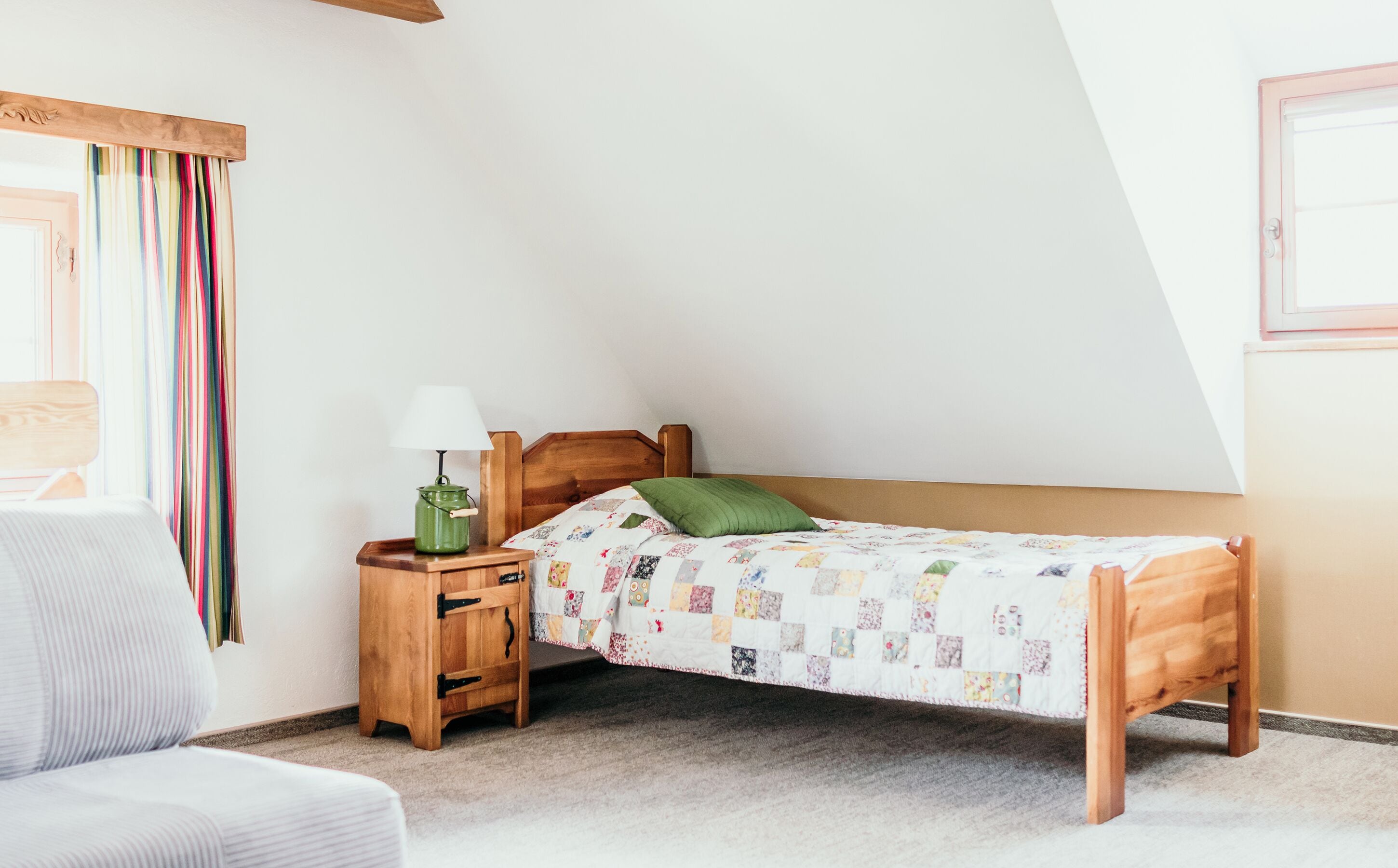 Un dormitorio con una cama de madera, una mesita de noche con lámpara, una silla y una cortina colorida.